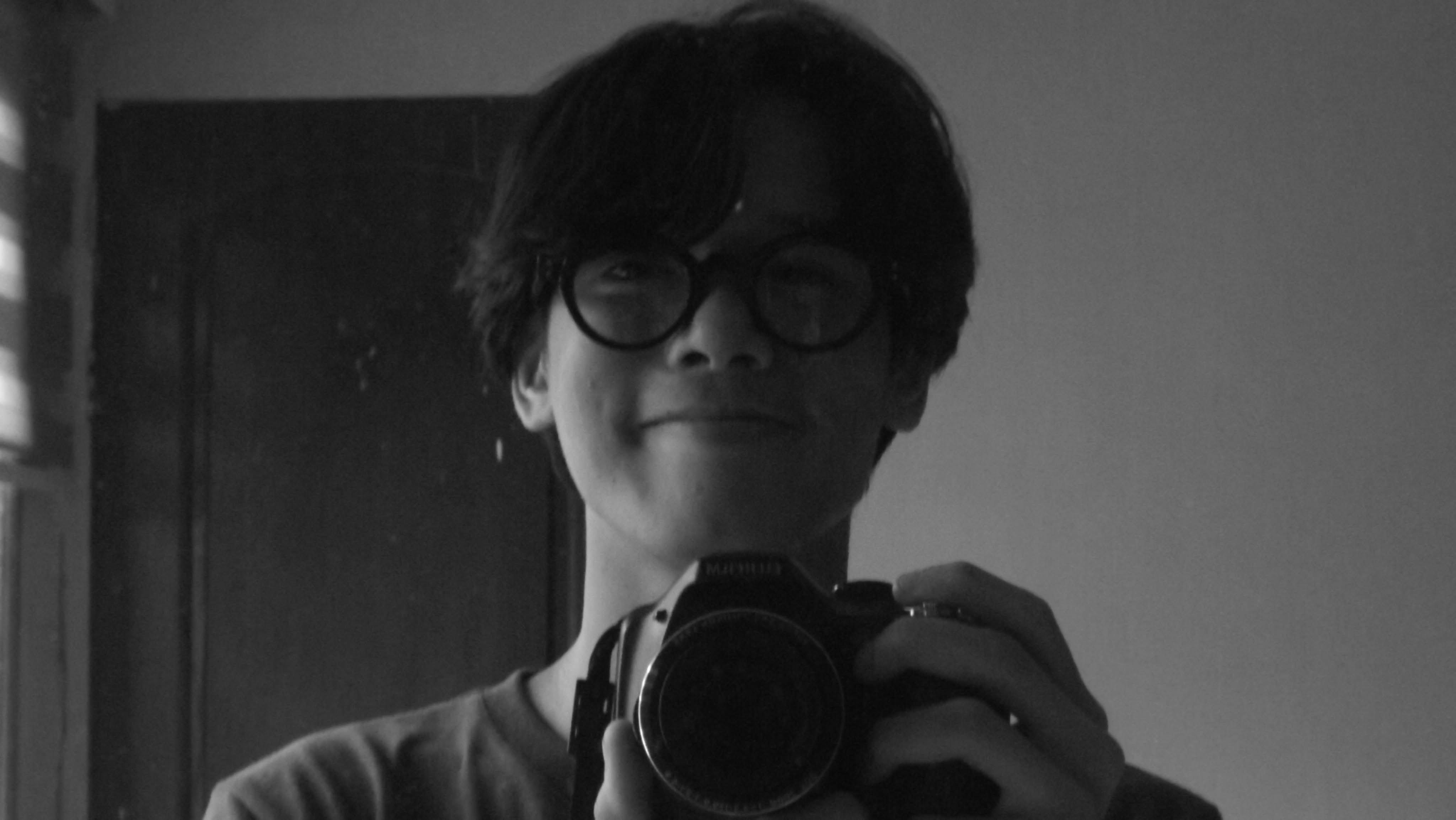 Black-and-white mirror portrait of jucu holding a film camera to his chest